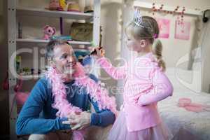 Smiling daughter in fairy costume putting makeup on her fathers face