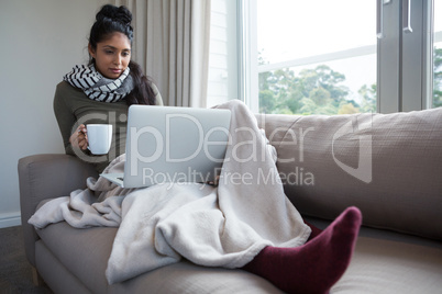 Full length of woman with coffee cup looking into laptop
