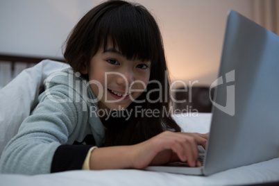 Portrait of smiling girl using laptop on bed