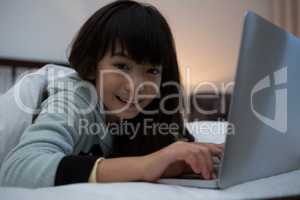 Portrait of smiling girl using laptop on bed