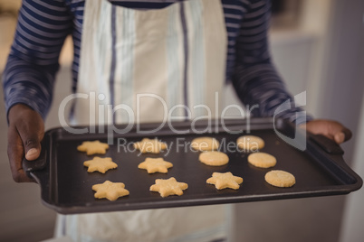 Man holding tray of cookies in kitchen