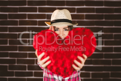 Smiling woman showing heart shape against brick wall