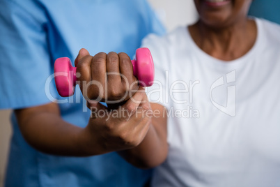 Midsection of nurse guiding senior woman in lifting dumbbell