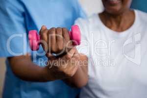 Midsection of nurse guiding senior woman in lifting dumbbell