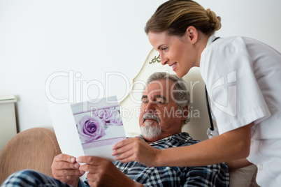 Female doctor showing get well card to patient relaxing on bed
