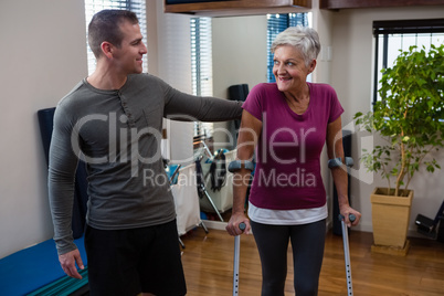 Physiotherapist assisting senior woman patient to walk with crutches