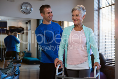 Physiotherapist assisting senior patient to walk with walking frame
