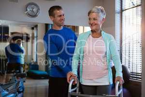 Physiotherapist assisting senior patient to walk with walking frame