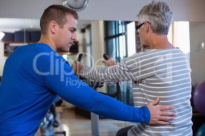 Physiotherapist assisting senior woman in performing exercise on exercise bike