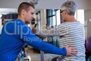 Physiotherapist assisting senior woman in performing exercise on exercise bike