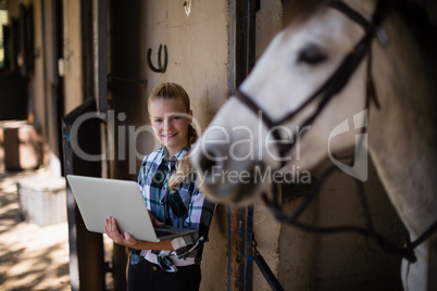 Teenage girl using laptop in the stable