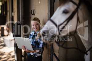 Teenage girl using laptop in the stable