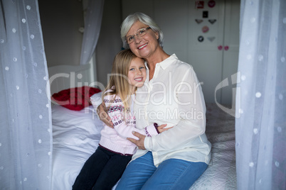 Smiling grandmother and granddaughter sitting together on bed