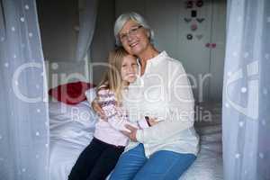 Smiling grandmother and granddaughter sitting together on bed