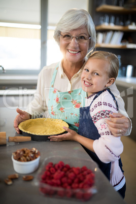Smiling grandmother and granddaughter posing while making pie
