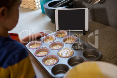 Boy holding muffin tin with cupcake holders at kitchen counter
