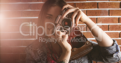 Woman photographing from vintage camera against brick wall
