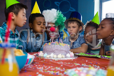 children with clown blowing candles on cake