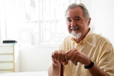Portrait of happy senior man holding walking cane in nursing home