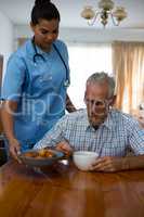 Doctor serving food to senior man at table in nursing home