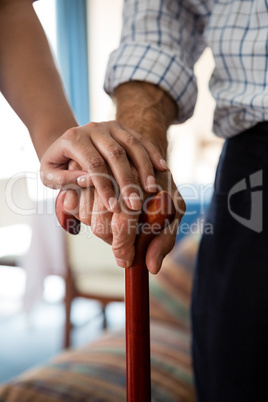 Hands of female doctor and senior man holding walking cane in retirement home
