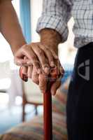 Hands of female doctor and senior man holding walking cane in retirement home