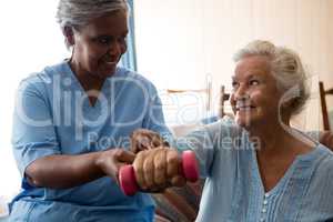 Nurse helping senior woman in lifting dumbell