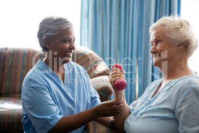 Smiling nurse looking at senior woman lifting dumbell