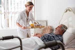 Female doctor serving food to senior patient relaxing on bed