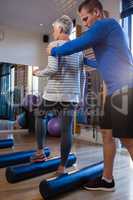 Physiotherapist assisting senior woman in performing exercise on foam roll