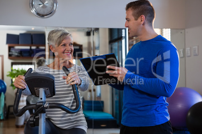 Physiotherapist interacting with senior woman while exercising on exercise bike