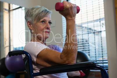 Senior woman in wheelchair performing exercise with dumbbell