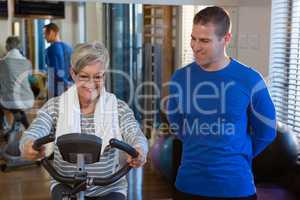 Physiotherapist assisting senior woman in performing exercise on exercise bike