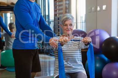 Physiotherapist assisting senior woman in performing stretching exercise with resistance band