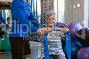Physiotherapist assisting senior woman in performing stretching exercise with resistance band