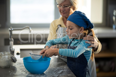 Grandmother assisting granddaughter to sieve the flour