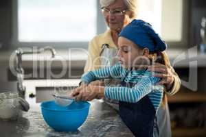 Grandmother assisting granddaughter to sieve the flour