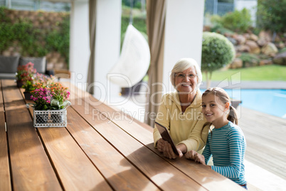 Granddaughter and grandmother sitting in a deck shade with a digital tablet