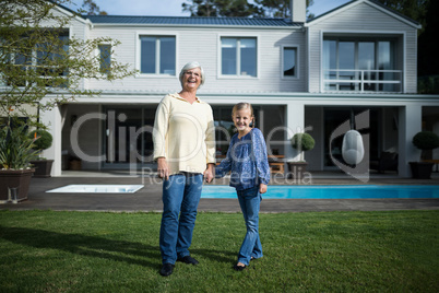 Smiling granddaughter and grandmother standing in garden