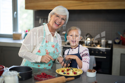 Grandmother and granddaughter posing while adding blue berries to the crust