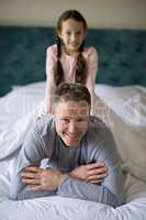 Smiling daughter sitting on fathers back in bedroom