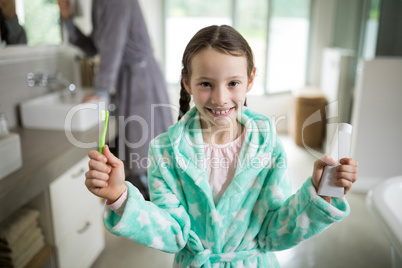 Smiling girl holding toothpaste and toothbrush in bathroom