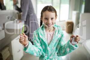 Smiling girl holding toothpaste and toothbrush in bathroom