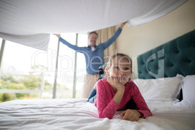 Father spreading a white blanket over his daughter