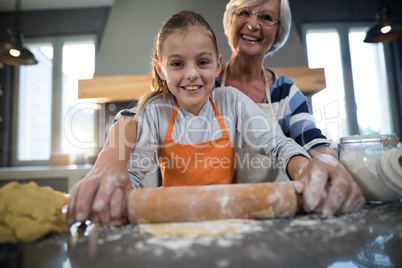 Grandmother and granddaughter posing while flattening dough