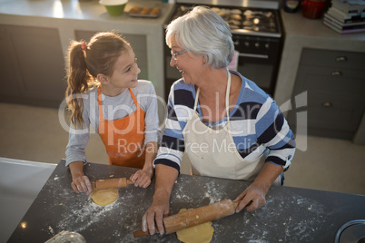 Grandmother and granddaughter looking at each other while flattening dough