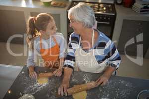 Grandmother and granddaughter looking at each other while flattening dough