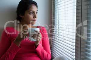 Thoughtful woman with coffee cup by window