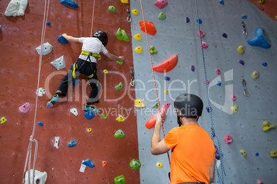 Trainer assisting boy in rock climbing