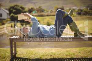 Senior woman reading a book while lying on the bench in the park